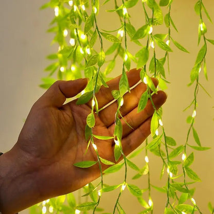 Hand holding a green leafy plant with small lights against a neutral background